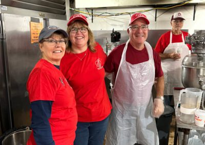 Three people in red shirts and aprons standing in a kitchen, preparing food together.